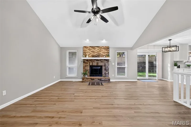 Vaulted ceiling with a ceiling fan, brick fireplace, wood-finish flooring, and white painted walls — 341 Westbrook Drive, O'Fallon, MO 63366