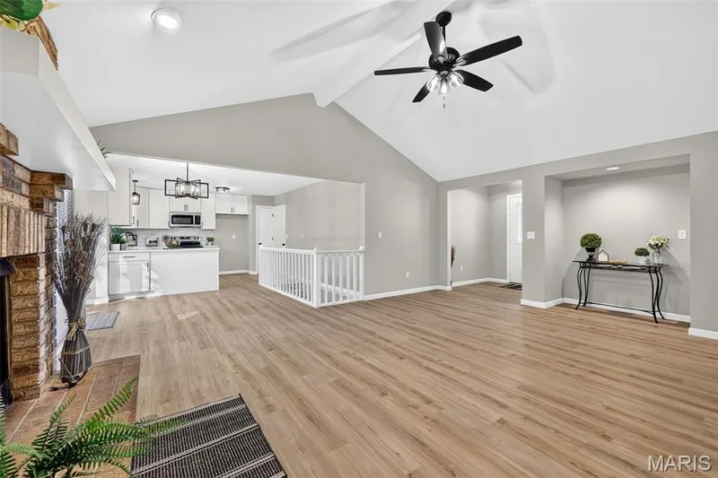Vaulted ceilings featuring a ceiling fan, wood-finish flooring, a brick fireplace, white kitchen cabinetry, and built-in kitchen appliances — 341 Westbrook Drive, O'Fallon, MO 63366