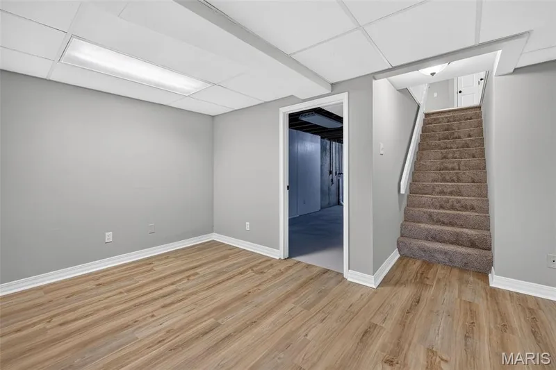 Expansive room featuring wood-finish flooring, light gray wall paint, white trim, and a drop ceiling with integrated lighting — 341 Westbrook Drive, O'Fallon, MO 63366