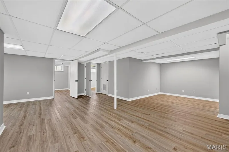 Spacious room featuring wood-finish flooring, light gray walls, white trim, and a drop ceiling with integrated lighting — 341 Westbrook Drive, O'Fallon, MO 63366