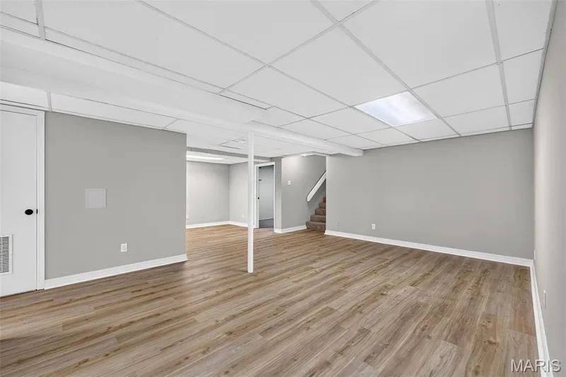 Spacious basement featuring wood-finish flooring throughout, recessed ceiling lighting, and multiple support columns — 341 Westbrook Drive, O'Fallon, MO 63366