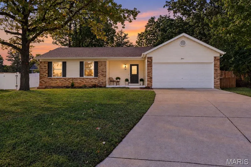 Exterior featuring brick and siding facade, a two-car garage, a concrete driveway, a front entry with sidelights, and mature trees — 341 Westbrook Drive, O'Fallon, MO 63366