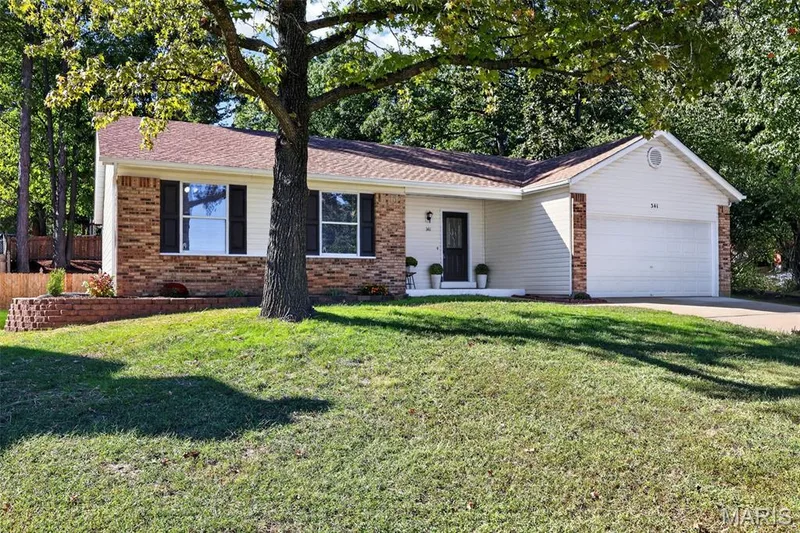 Exterior featuring brick and siding facade, an attached garage, a front entry, a sloped shingle roof, and a mature tree — 341 Westbrook Drive, O'Fallon, MO 63366
