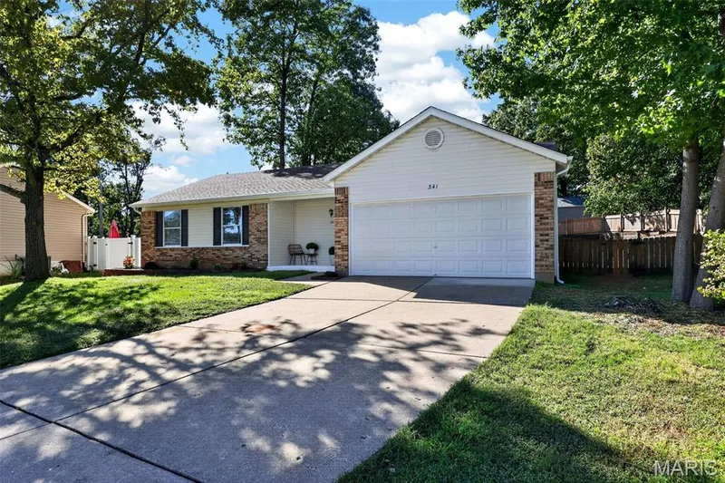 Charming brick ranch home featuring a two-car attached garage, professional driveway, and manicured lawn framed by mature shade trees — 341 Westbrook Drive, O'Fallon, MO 63366
