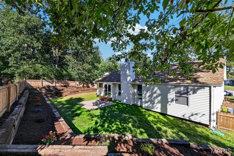 Expansive backyard featuring a privacy fence, tiered landscaping, a paved patio, and mature trees — 341 Westbrook Drive, O'Fallon, MO 63366