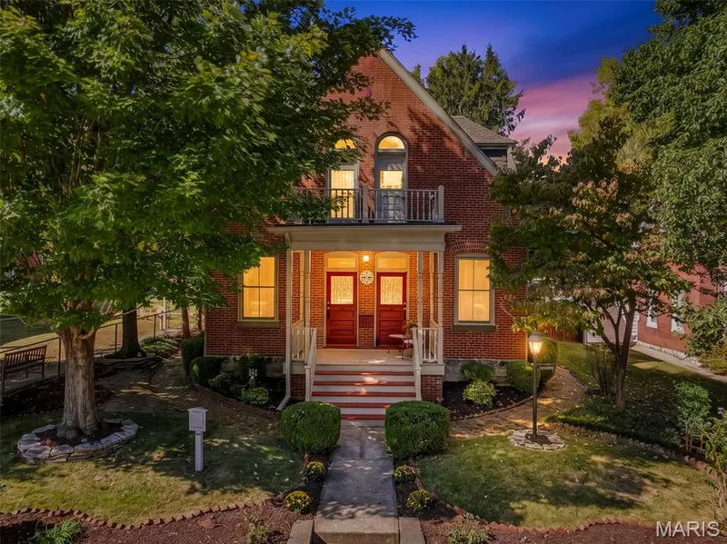 Brick exterior featuring a covered front porch, arched window detailing, an upper-level balcony, and mature landscaping — 711 N 5th Street, St Charles, MO 63301