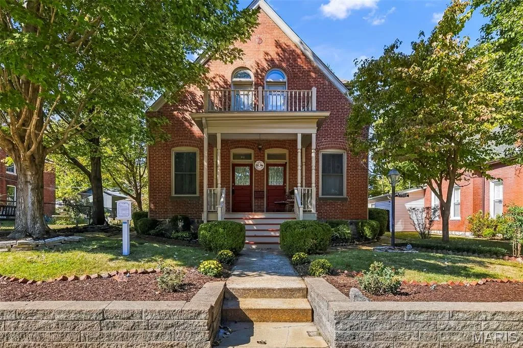 Brick exterior featuring a covered front porch, decorative upper-level balcony, and structured stone retaining wall — 711 N 5th Street, St Charles, MO 63301