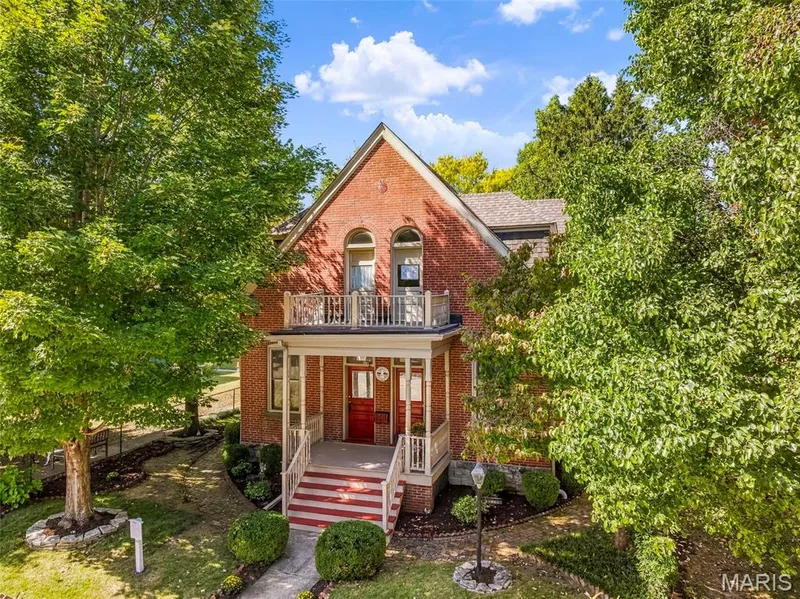 Brick exterior featuring an arched entryway, decorative porch railing, upper-level balcony, and gabled roofline — 711 N 5th Street, St Charles, MO 63301