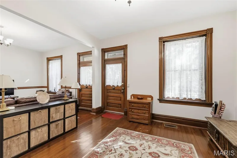Interior space featuring natural wood-finish flooring, original stained wood door and window casings, and a transom window above the entrance — 711 N 5th Street, St Charles, MO 63301