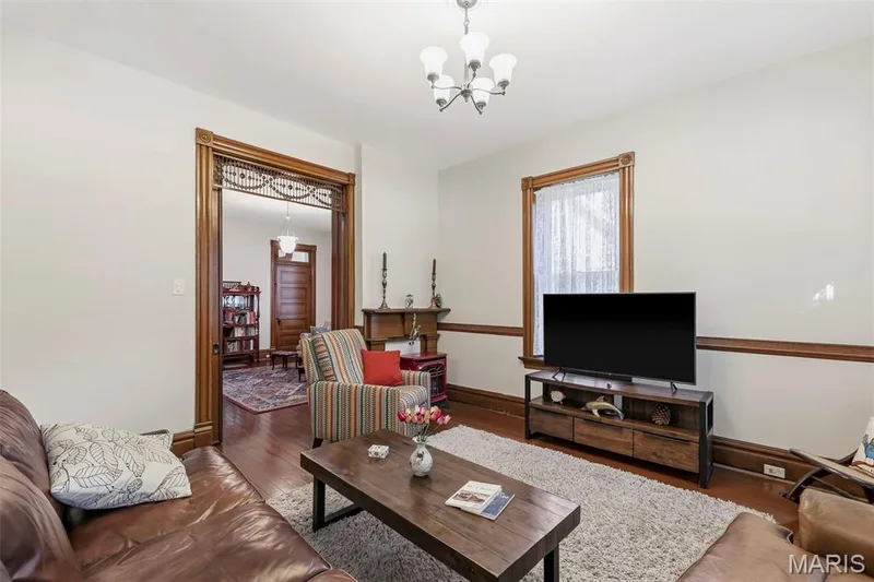 Interior room featuring rich wood-finish trim, decorative wood door casing with transom detail, dark wood-finish flooring, chair rail molding, and an overhead multi-light chandelier — 711 N 5th Street, St Charles, MO 63301