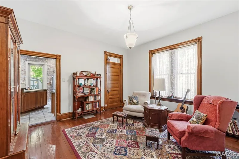 Interior room featuring natural wood-finish flooring, original stained wood door and window casing, five-panel wood door with a transom window, and a milk glass pendant light fixture — 711 N 5th Street, St Charles, MO 63301