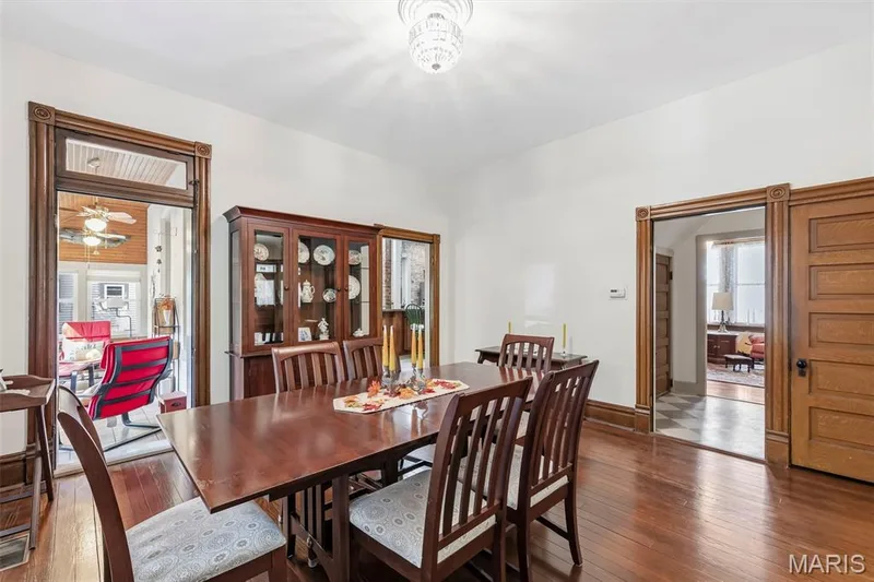 Dining area featuring original wood-trim door casings, solid wood-finish flooring, a tiered crystal-style chandelier, and paneled wood doors — 711 N 5th Street, St Charles, MO 63301