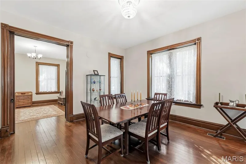 Interior space featuring natural wood-finish flooring, original stained wood door and window casing with decorative plinth blocks, and a crystal-style flush-mount ceiling fixture — 711 N 5th Street, St Charles, MO 63301