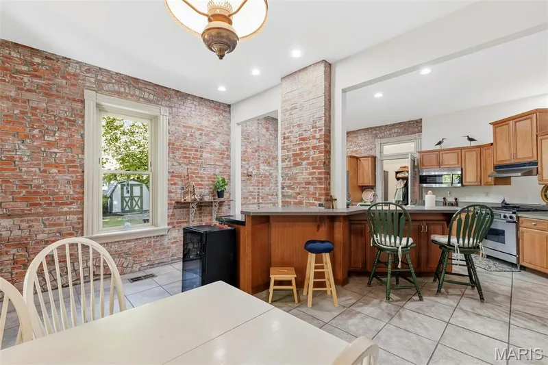 Exposed brick interior walls featuring a built-in kitchen peninsula, tile flooring, and custom cabinetry with stainless steel appliances — 711 N 5th Street, St Charles, MO 63301