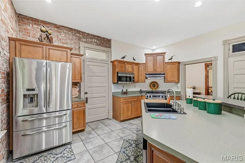 Kitchen featuring exposed brick walls, wood cabinetry, a central island with a double-basin sink, and tile flooring — 711 N 5th Street, St Charles, MO 63301