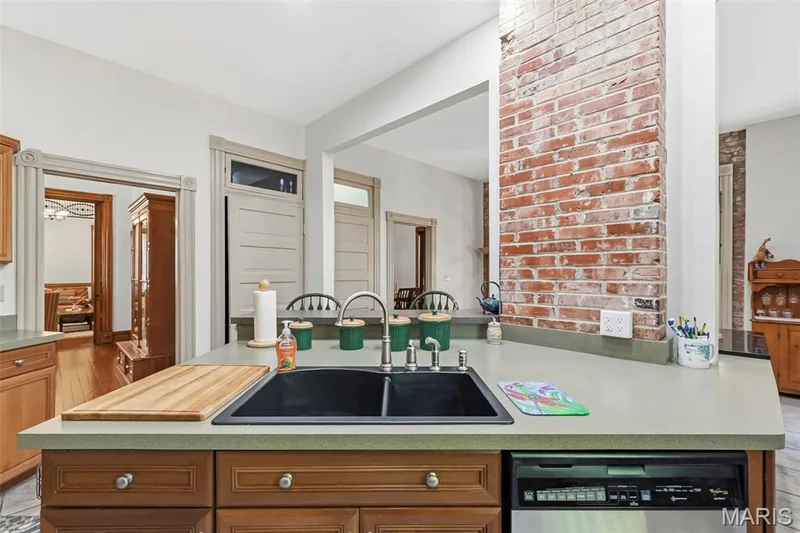 Kitchen featuring a center island with a dual-basin drop-in sink, high-arch faucet, solid-surface countertops, and an exposed brick structural column — 711 N 5th Street, St Charles, MO 63301