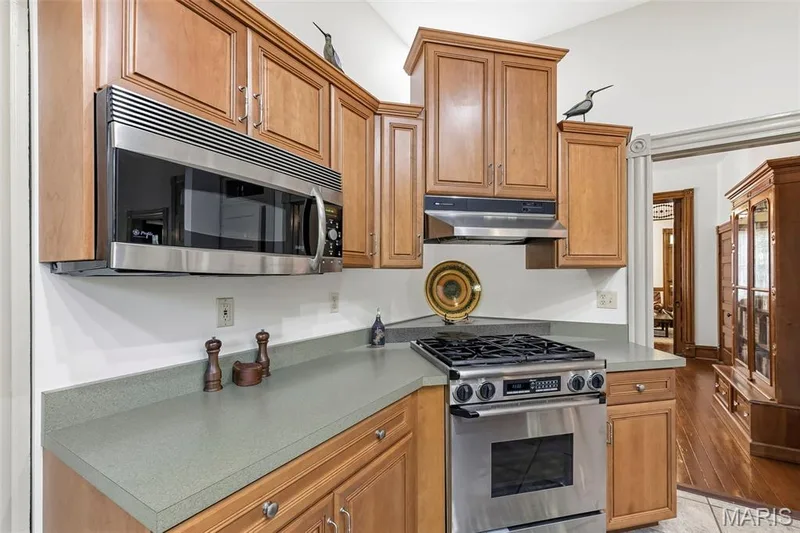 Kitchen featuring wood cabinetry, stainless steel microwave and gas range, and solid-surface countertops — 711 N 5th Street, St Charles, MO 63301
