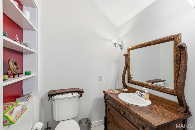 Built-in recessed shelving, vanity cabinet with wood finish, oval drop-in sink, decorative mirror, and wall-mounted light fixture — 711 N 5th Street, St Charles, MO 63301
