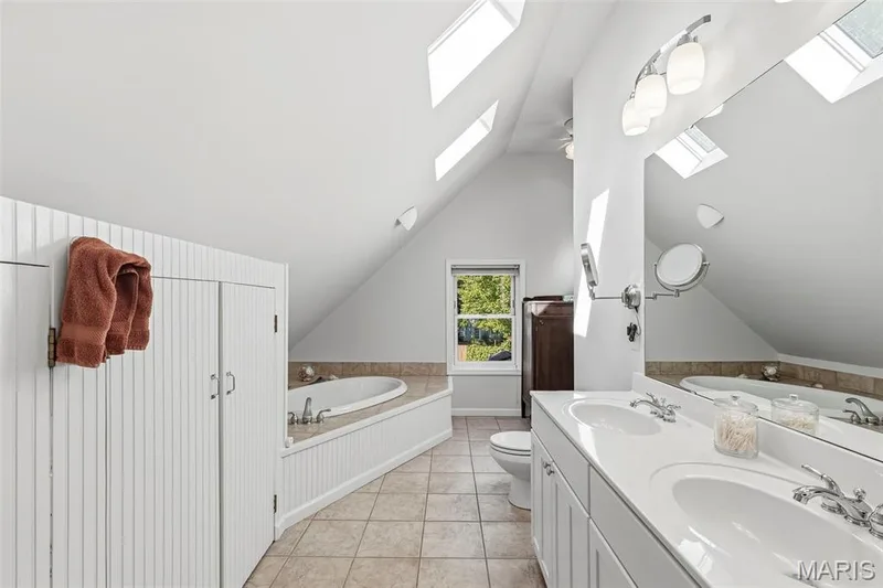 Bathroom featuring a double vanity with an expansive mirror, a recessed soaking tub with beadboard surround, multiple skylights, and tile flooring — 711 N 5th Street, St Charles, MO 63301