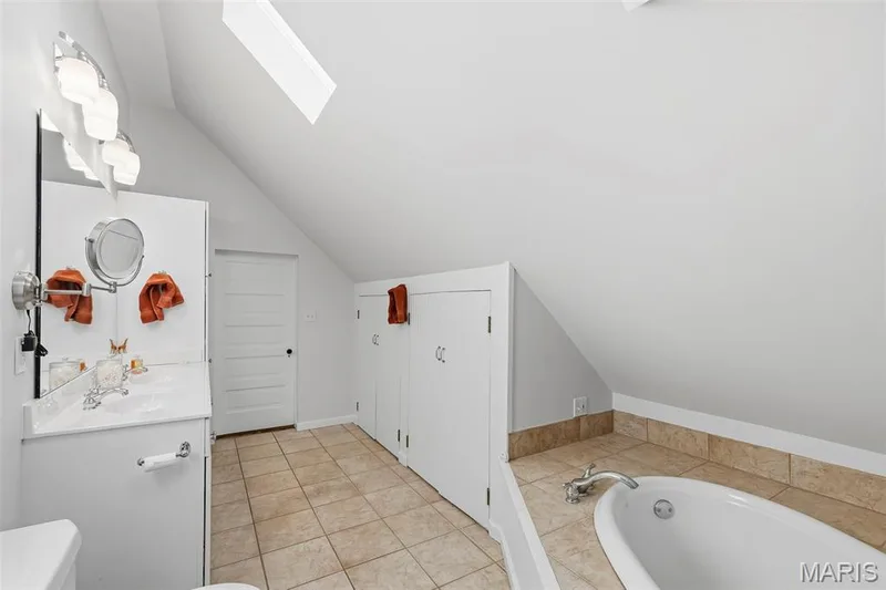 Bathroom featuring vaulted ceilings, a skylight, a built-in soaking tub with tile surround, a white vanity, and built-in knee-wall storage cabinets — 711 N 5th Street, St Charles, MO 63301