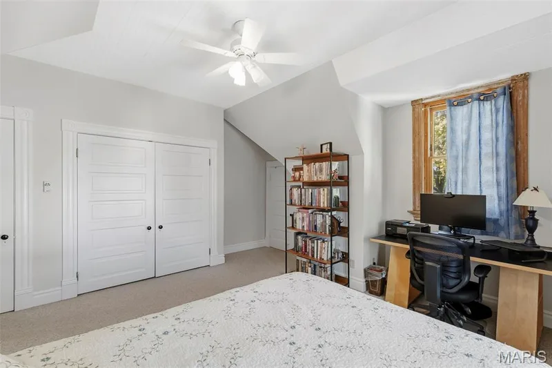 Neutral-toned room featuring slanted ceiling lines, white paneled double closet doors, white trim, and a multi-pane window with wood framing — 711 N 5th Street, St Charles, MO 63301