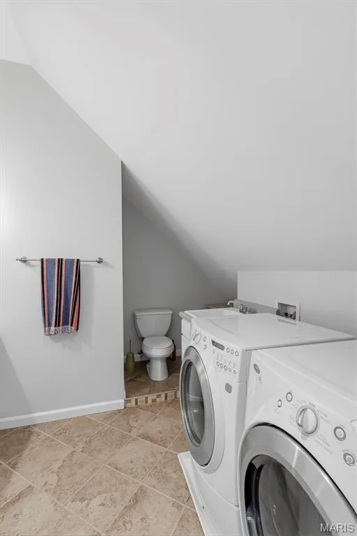Utility room featuring stone-tile flooring, a white porcelain toilet, and a built-in white vanity cabinet with an integrated sink — 711 N 5th Street, St Charles, MO 63301