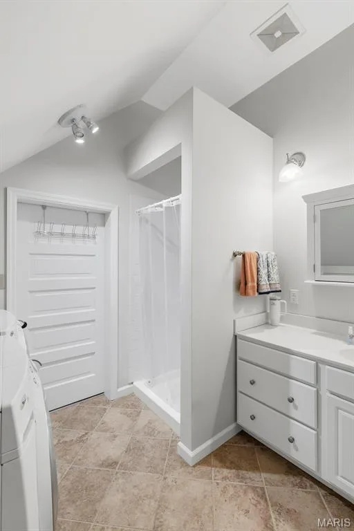 Bathroom featuring a vaulted ceiling, tiled flooring, white built-in cabinetry with a stone-finish countertop, a shower with a curtain enclosure, and wall-mounted light fixtures — 711 N 5th Street, St Charles, MO 63301