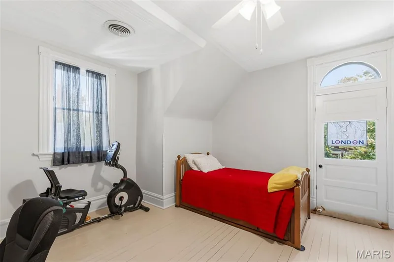 Room featuring painted wood-plank flooring, vaulted ceiling, ceiling fan, sash window with decorative molding, and an exterior door with a glass transom — 711 N 5th Street, St Charles, MO 63301
