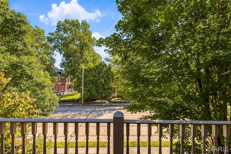 balcony featuring a wooden balustrade and railings, overlooking mature trees and street-level landscape — 711 N 5th Street, St Charles, MO 63301