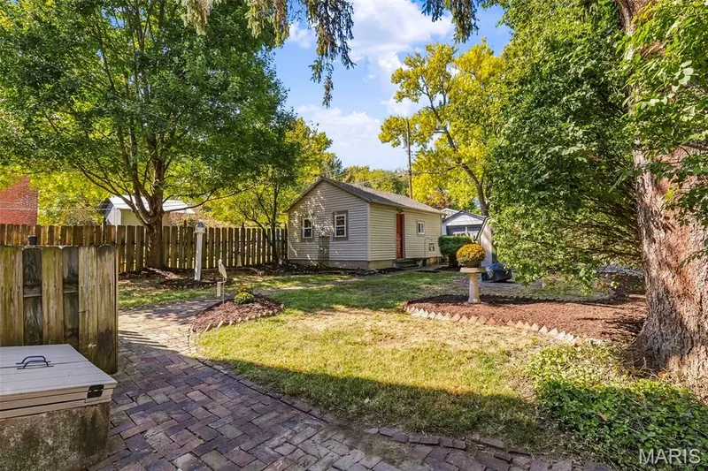 Private backyard featuring a brick paver patio, wood privacy fencing, mulched landscape beds, and mature trees — 711 N 5th Street, St Charles, MO 63301