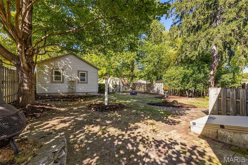 Backyard featuring stone paver hardscaping, mature shade trees, detached storage structure, and perimeter wood fencing — 711 N 5th Street, St Charles, MO 63301