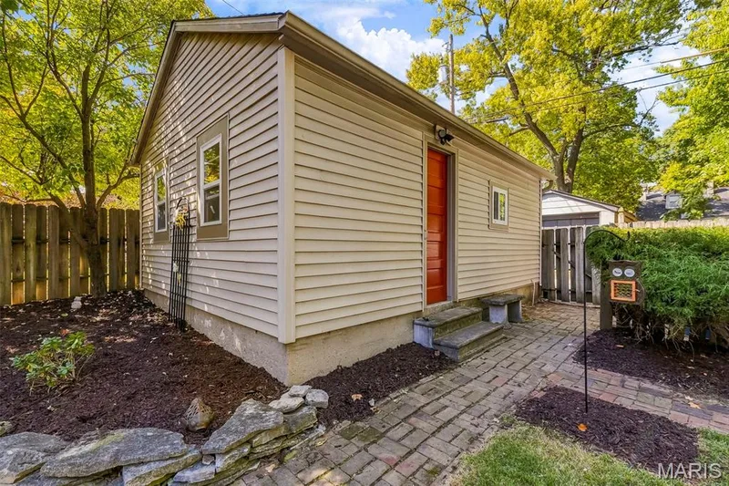 Garage, beige vinyl siding, a red entry door, a brick paver walkway, and stone-bordered landscaping — 711 N 5th Street, St Charles, MO 63301