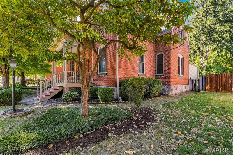 Red brick exterior featuring a covered front porch with decorative railings, stone foundation, and natural stone walkways — 711 N 5th Street, St Charles, MO 63301