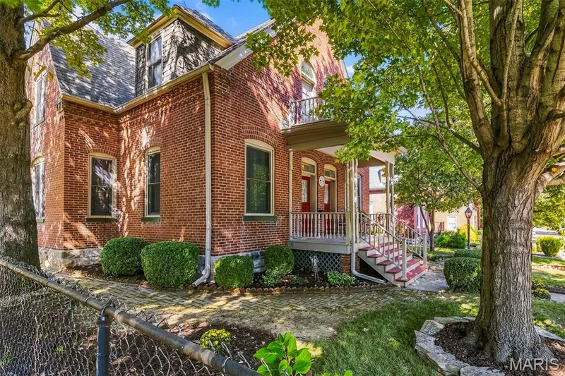 Red brick exterior featuring a covered front porch, stone foundation accents, a second-story balcony, and arched window detailing — 711 N 5th Street, St Charles, MO 63301