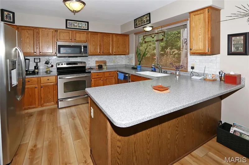 Wood-finish flooring, stainless steel appliances, white tile backsplash, light wood cabinetry, and a double basin sink — 1738 Sun Drop Drive, St Charles, MO 63303