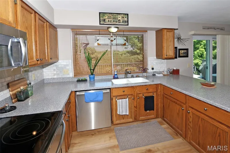 Wood-finish flooring with a U-shaped countertop layout, white subway tile backsplash, and wood cabinetry — 1738 Sun Drop Drive, St Charles, MO 63303