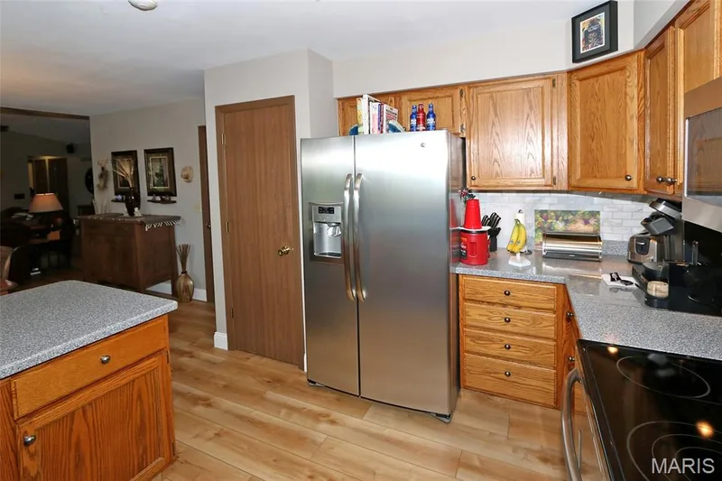 Stainless steel refrigerator, wood-finish flooring, wood cabinetry, light-toned countertops, and a subway tile backsplash — 1738 Sun Drop Drive, St Charles, MO 63303