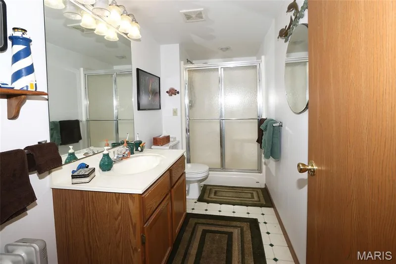 Wood-finish vanity with an integrated sink, large wall-mounted mirror, and a shower with sliding glass doors — 1738 Sun Drop Drive, St Charles, MO 63303