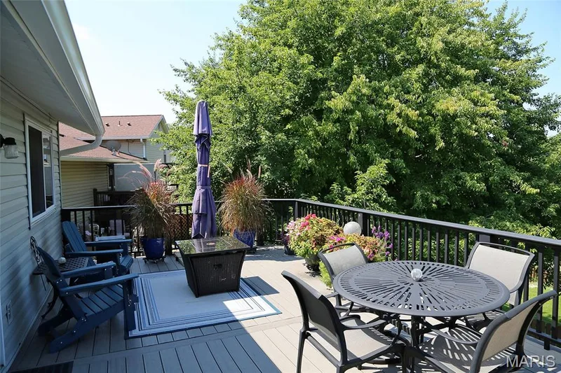 Expansive exterior deck featuring a composite surface, dark railings, and mature surrounding trees — 1738 Sun Drop Drive, St Charles, MO 63303