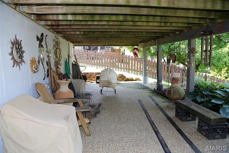 Covered outdoor patio with exposed wood joists, concrete flooring, and a partial white picket fence — 1738 Sun Drop Drive, St Charles, MO 63303