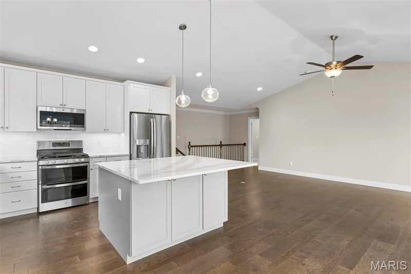 Kitchen with pendant lighting, lofted ceiling, white cabinetry, a kitchen island, and appliances with stainless steel finishes — 2 Maple at Elm Crossing, St Charles, MO 63301