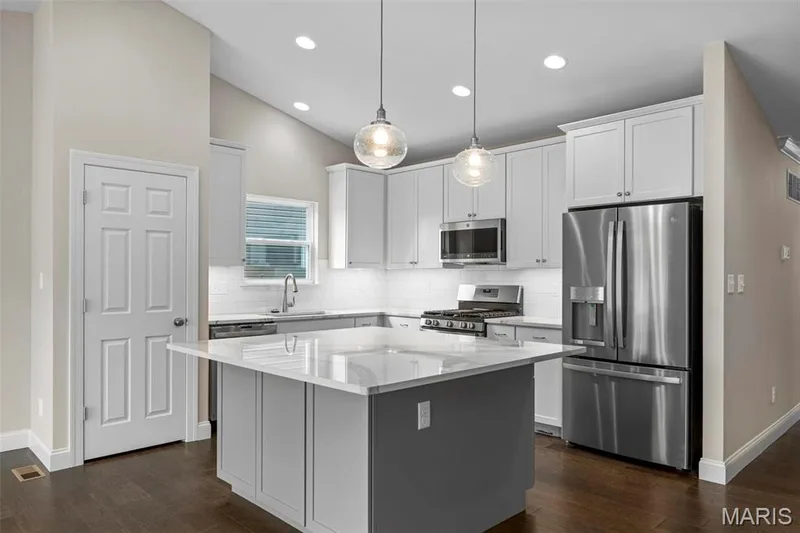 Kitchen featuring white cabinetry, appliances with stainless steel finishes, hanging light fixtures, and a kitchen island — 2 Maple at Elm Crossing, St Charles, MO 63301