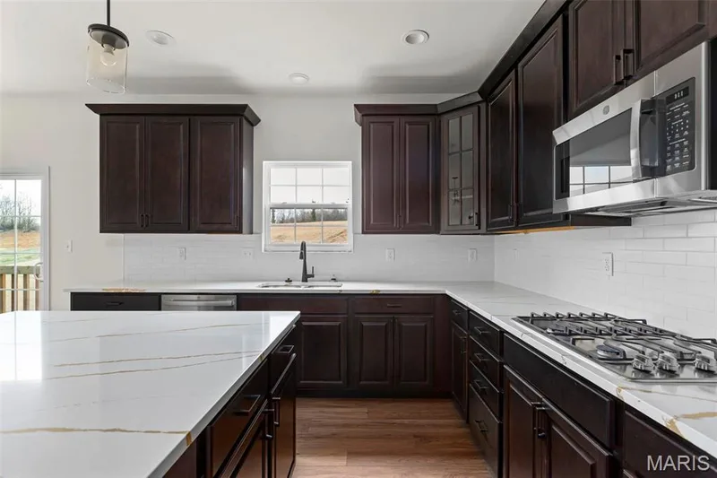 Kitchen with appliances with stainless steel finishes, tasteful backsplash, dark hardwood / wood-style flooring, dark brown cabinetry, and sink — 2 Sequoia at Elm Crossing, St Charles, MO 63301