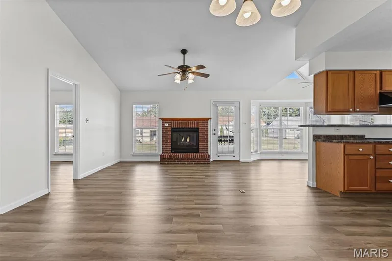 Expansive living space featuring wood-finish flooring, a brick fireplace, vaulted ceilings, and a ceiling fan — 2006 Chapel Hill Crossing, St Peters, MO 63376