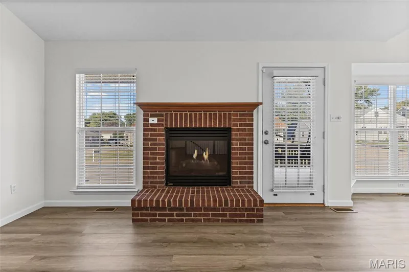 Brick fireplace with wood mantel, glass fireplace doors, wood-finish flooring, white walls, and white-framed windows — 2006 Chapel Hill Crossing, St Peters, MO 63376
