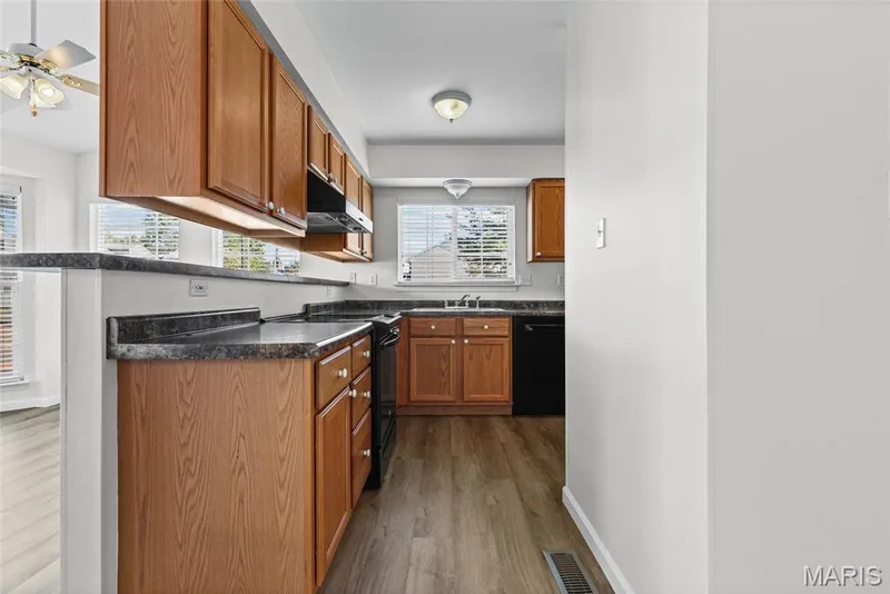 Wood-finish flooring, ample wood cabinetry, dark countertops, built-in appliances, and natural light from multiple windows — 2006 Chapel Hill Crossing, St Peters, MO 63376