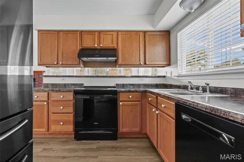 Kitchen featuring wood-finish cabinetry, dark countertops, a double-basin sink, and a black appliance suite — 2006 Chapel Hill Crossing, St Peters, MO 63376