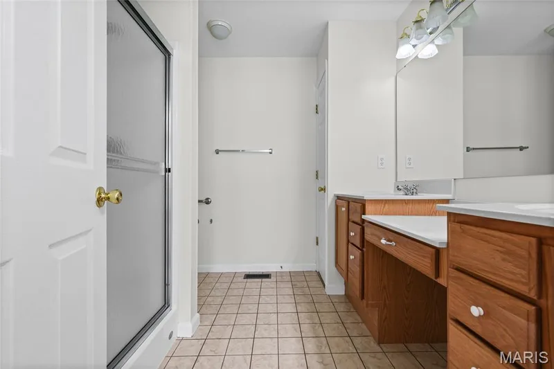 Bathroom featuring a glass-enclosed shower, wood-finish vanity cabinetry, dual sinks, and tile flooring — 2006 Chapel Hill Crossing, St Peters, MO 63376