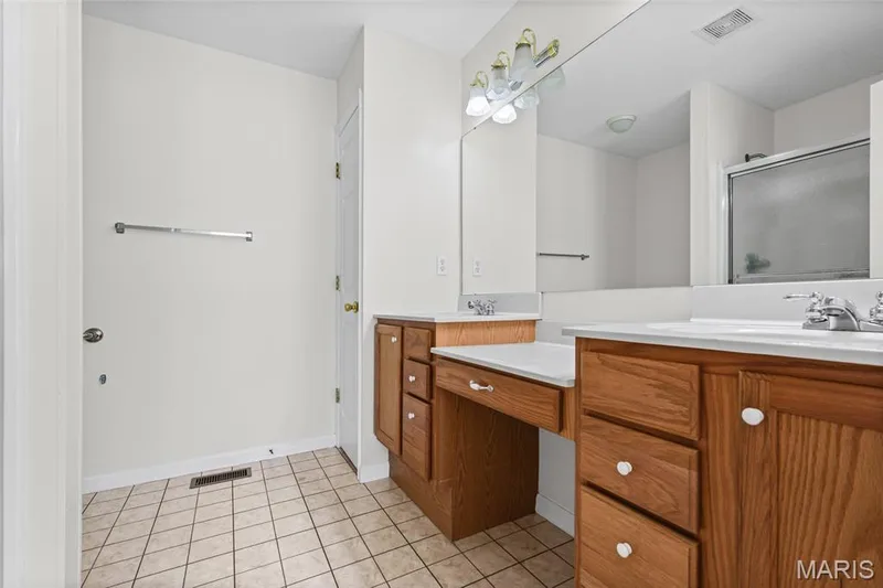 Dual vanity featuring wood cabinetry and integrated sinks, a built-in vanity area, tiled flooring, and a shower enclosure — 2006 Chapel Hill Crossing, St Peters, MO 63376