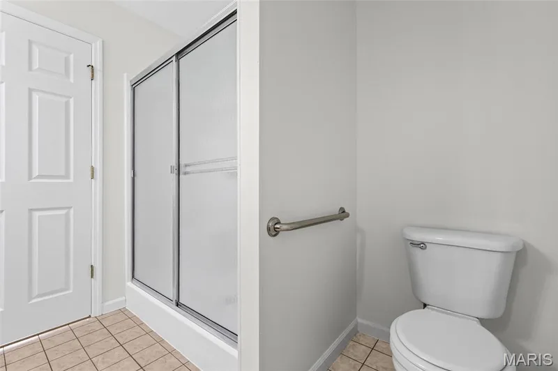 Tiled flooring, white paneled door, shower with sliding frosted glass doors, grab bar, and white toilet — 2006 Chapel Hill Crossing, St Peters, MO 63376